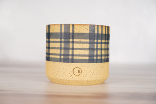 Blue plaid pattern candle on light brown speckled ceramic vessel, front view