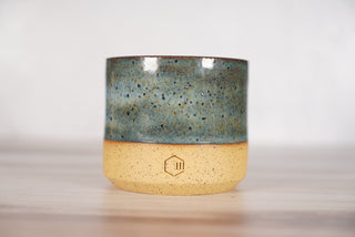 Rutile blue glaze candle on light brown ceramic vessel, front view