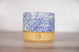 Speckled blue glaze candle on light brown ceramic vessel, front view
