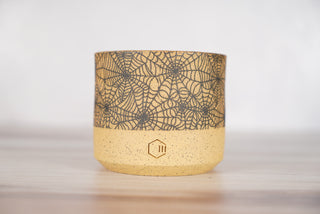 Spiderweb pattern candle on light brown speckled ceramic vessel, front view