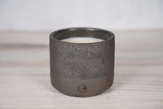 Black spiderweb pattern candle on dark brown speckled ceramic vessel, viewed from above