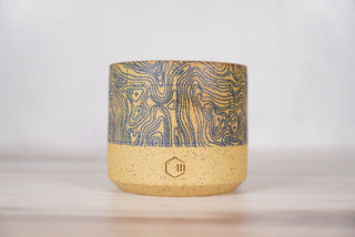 Blue topographic map pattern candle on light brown speckled ceramic vessel, front view
