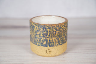 Blue topographic map pattern candle on light brown speckled ceramic vessel, viewed from above